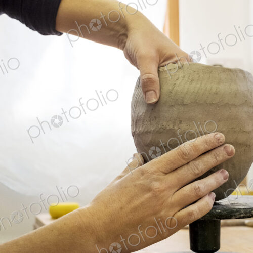 Close up of ceramic artist in her workshop, working on small clay vase.