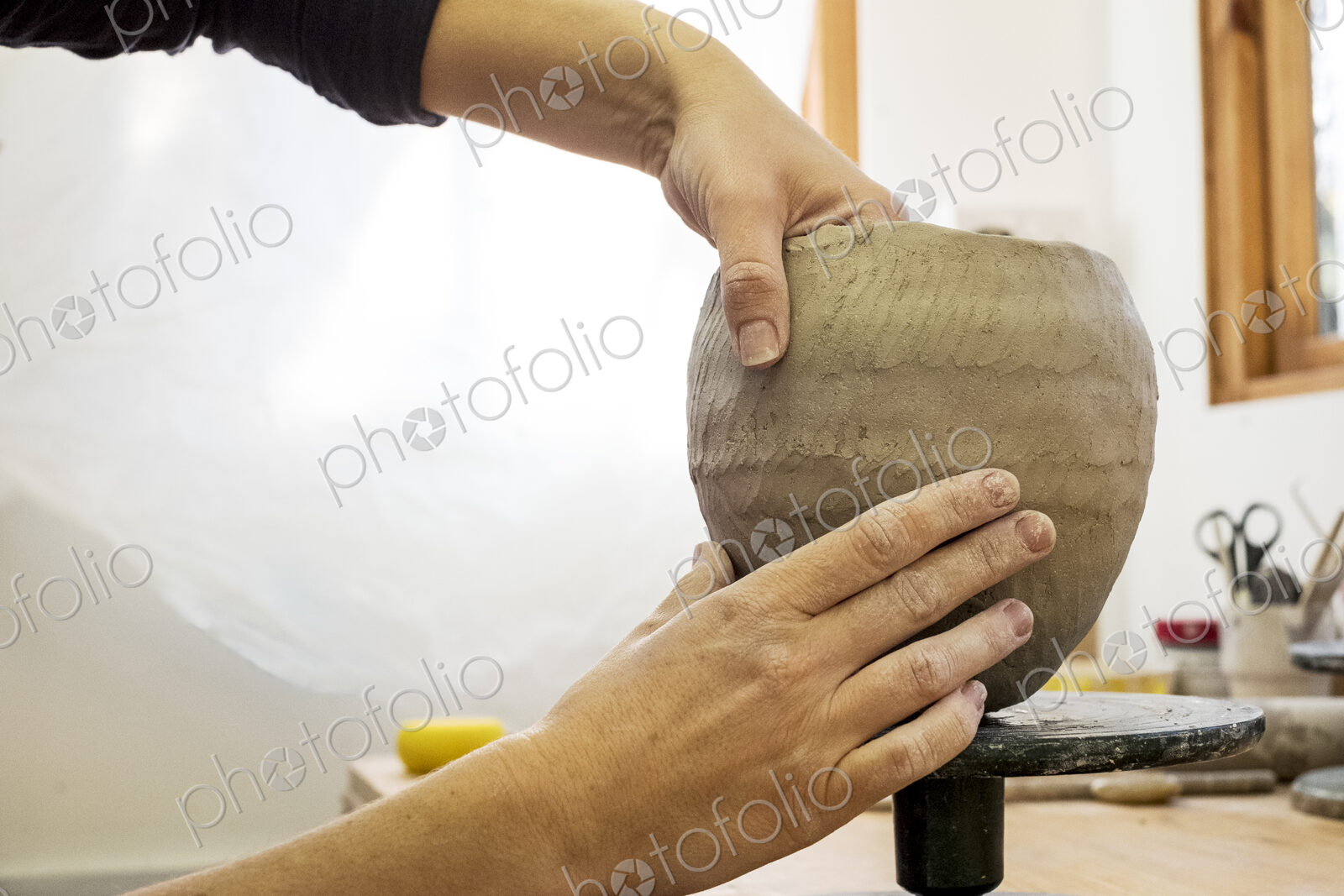 Close up of ceramic artist in her workshop, working on small clay vase.