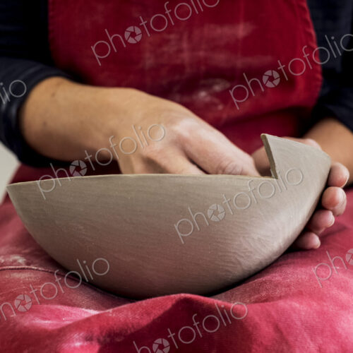 Close up of ceramic artist wearing red apron working on clay bowl.