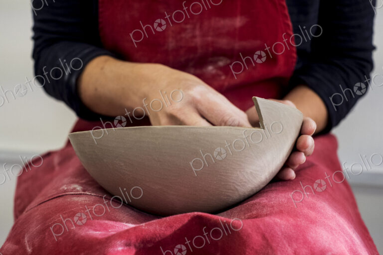 Close up of ceramic artist wearing red apron working on clay bowl.