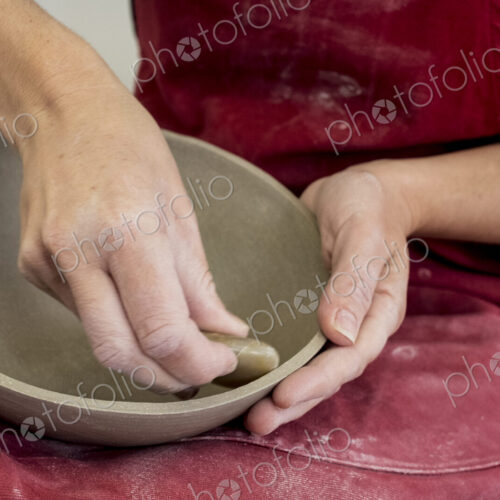 Close up of ceramic artist wearing red apron working on clay bowl.