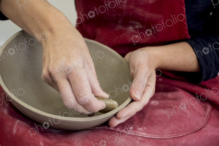 Close up of ceramic artist wearing red apron working on clay bowl.