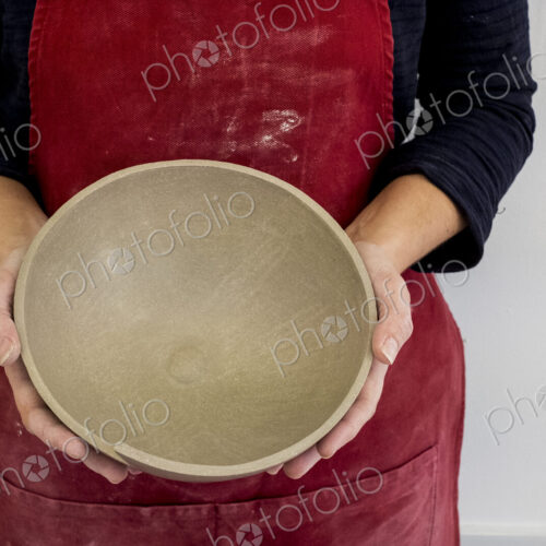 Close up of ceramic artist wearing red apron working on clay bowl.