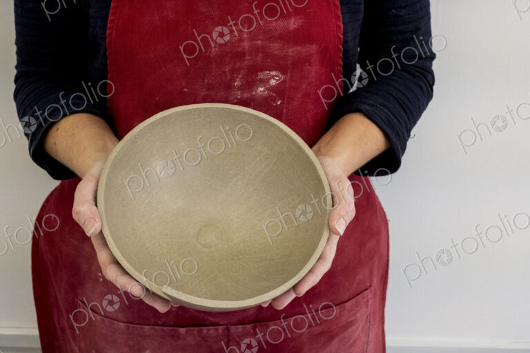 Close up of ceramic artist wearing red apron working on clay bowl.
