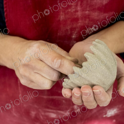 Close up of ceramic artist wearing red apron working on small clay bowl.