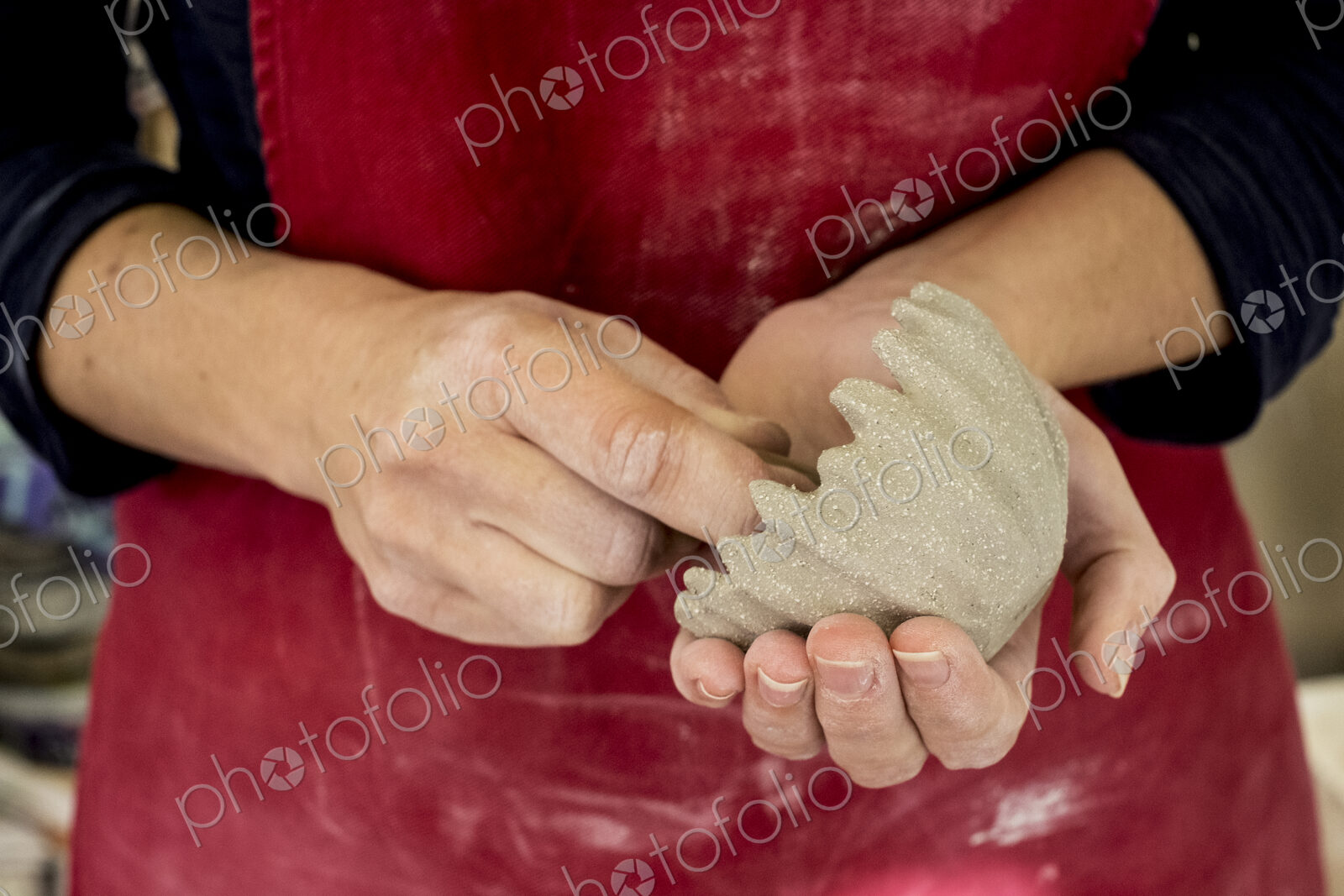 Close up of ceramic artist wearing red apron working on small clay bowl.