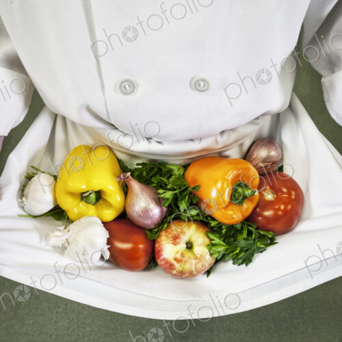 Close-up of chef holding an assortment of fresh vegetables in his apron. Close-up of chef holding an assortment of fresh vegetables in his apron.