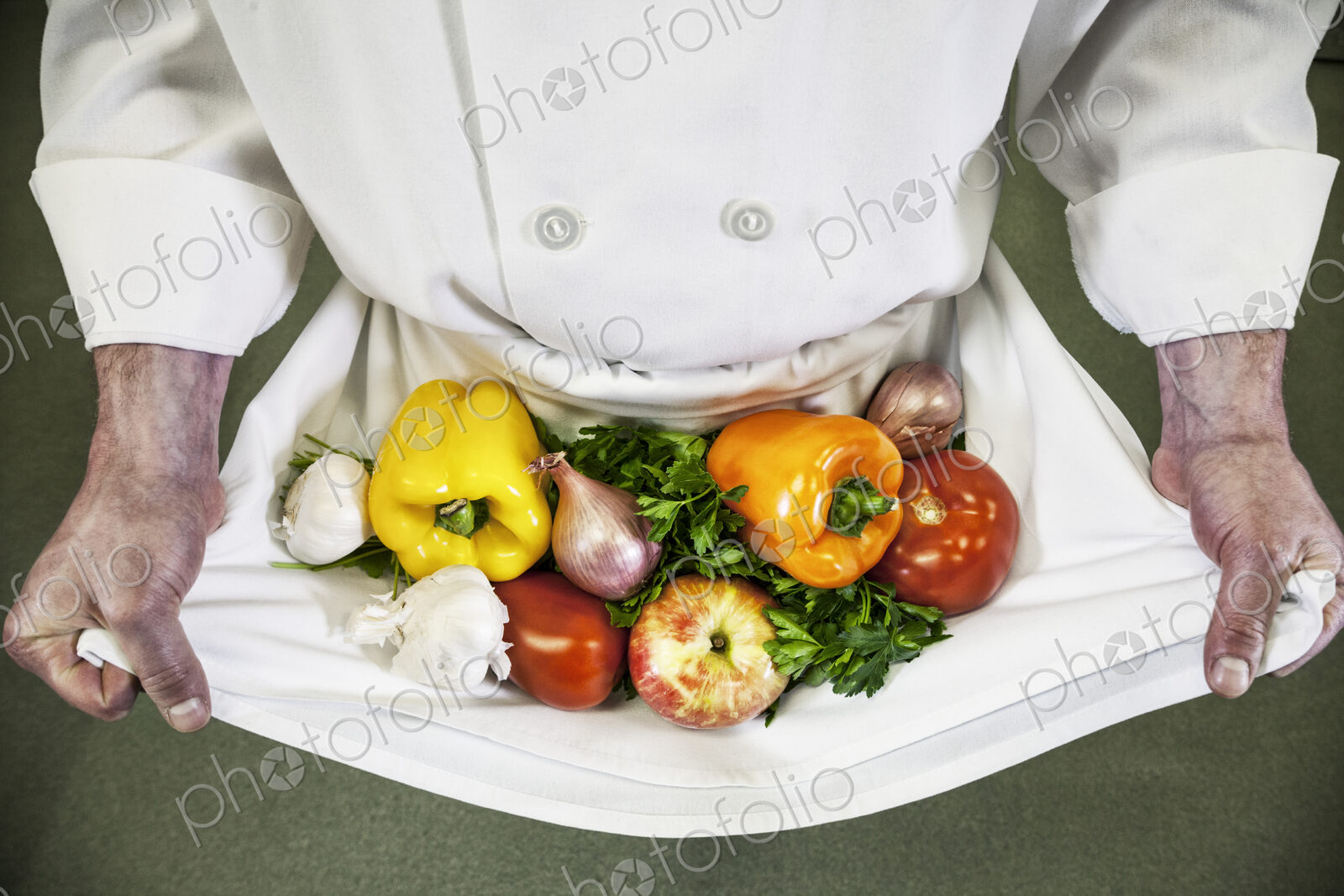 Close-up of chef holding an assortment of fresh vegetables in his apron.