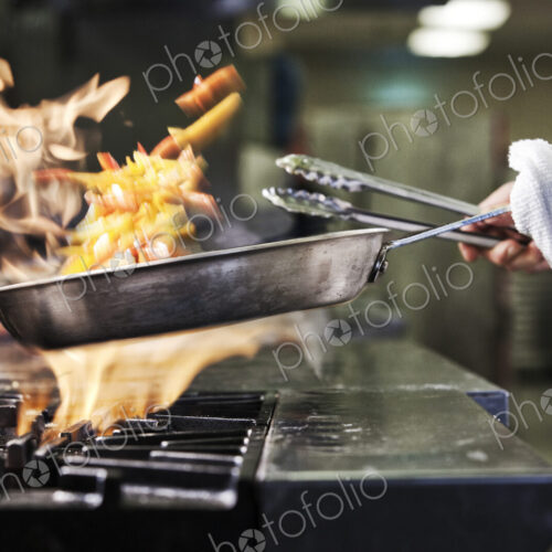Close-up of chef's hands holding a sauté pan to cook food, flambeing contents. Flames… Close-up of chef's hands holding a sauté pan to cook food, flambeing contents. Flames…