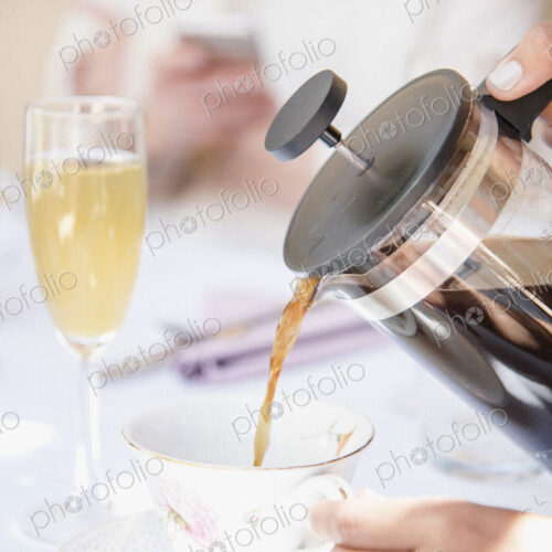 Close up of coffee being poured from a French Coffee Press into a cup, a glass of…