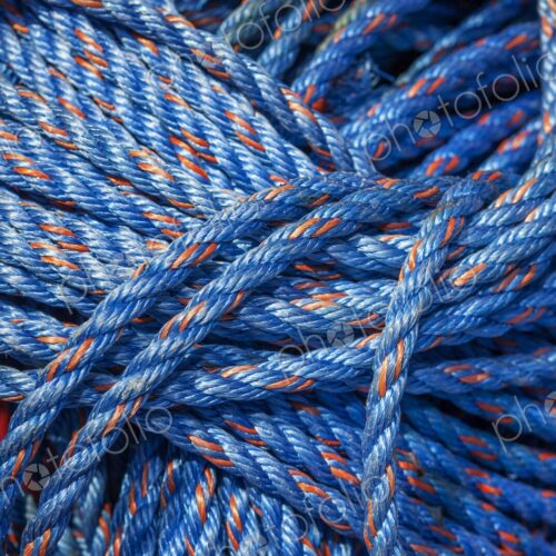 Close-up of coiled blue nylon rope with orange strands, tightly bundled and vibrant in…