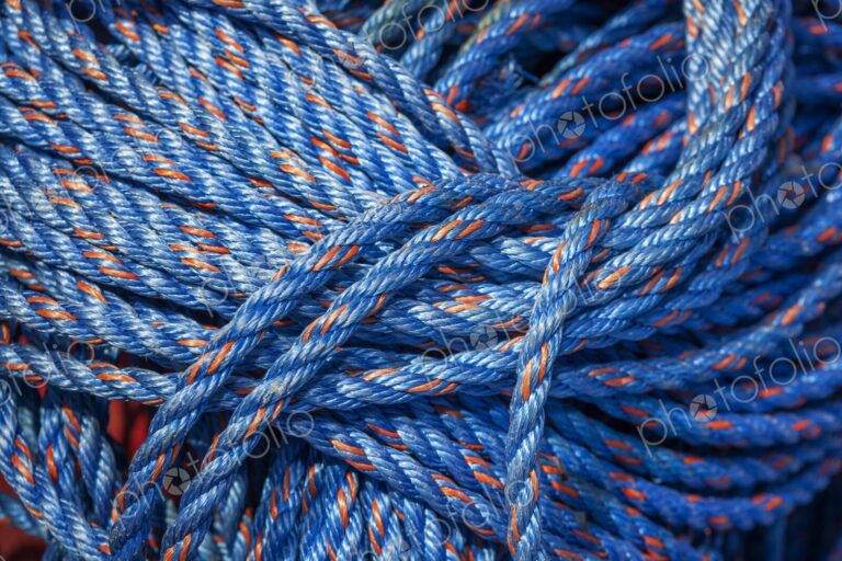 Close-up of coiled blue nylon rope with orange strands, tightly bundled and vibrant in…
