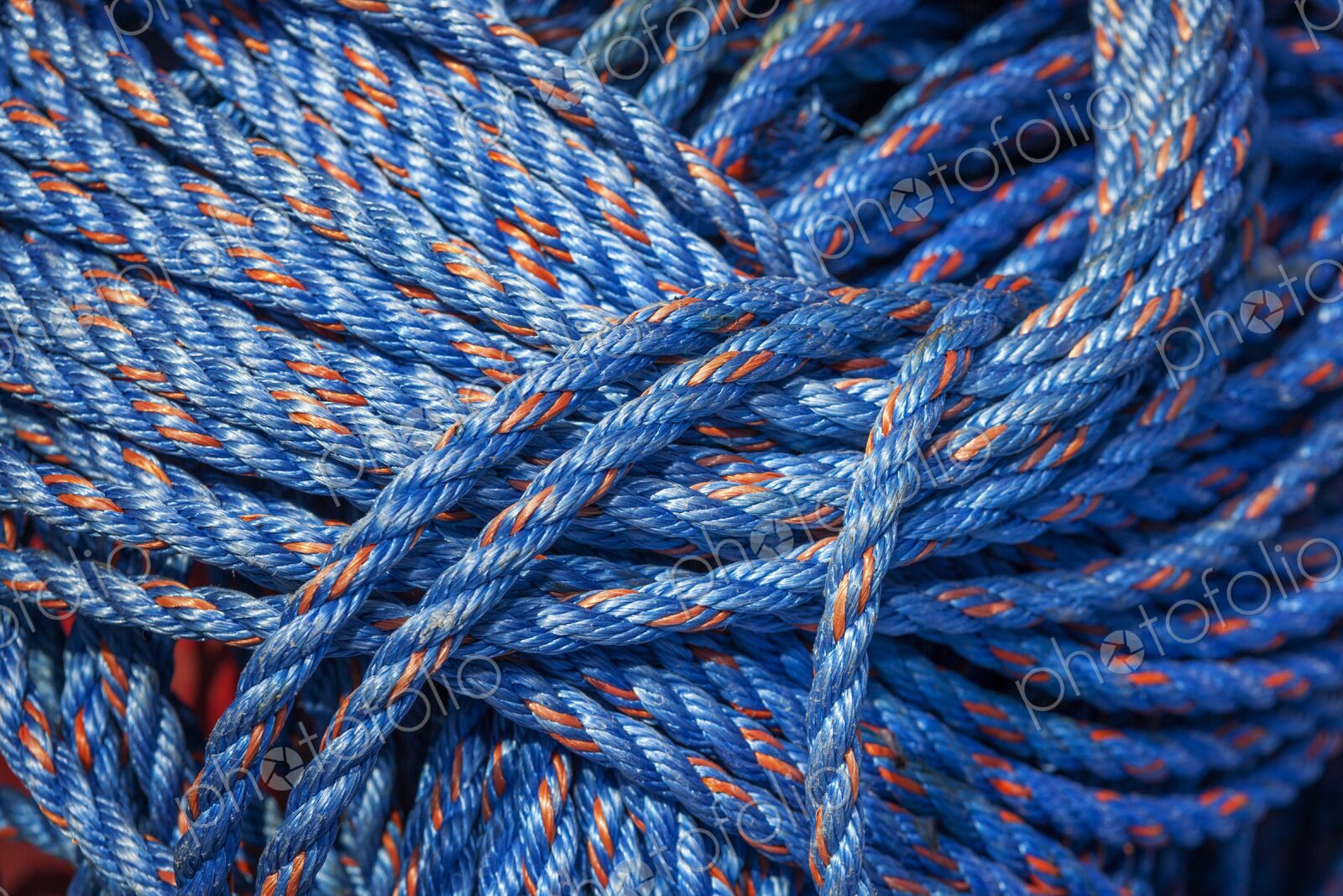 Close-up of coiled blue nylon rope with orange strands, tightly bundled and vibrant in…