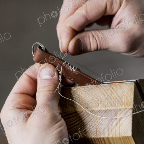 Close up of craftsman making brown leather camera strap, hand stitching two pieces of… Close up of craftsman making brown leather camera strap, hand stitching two pieces of…