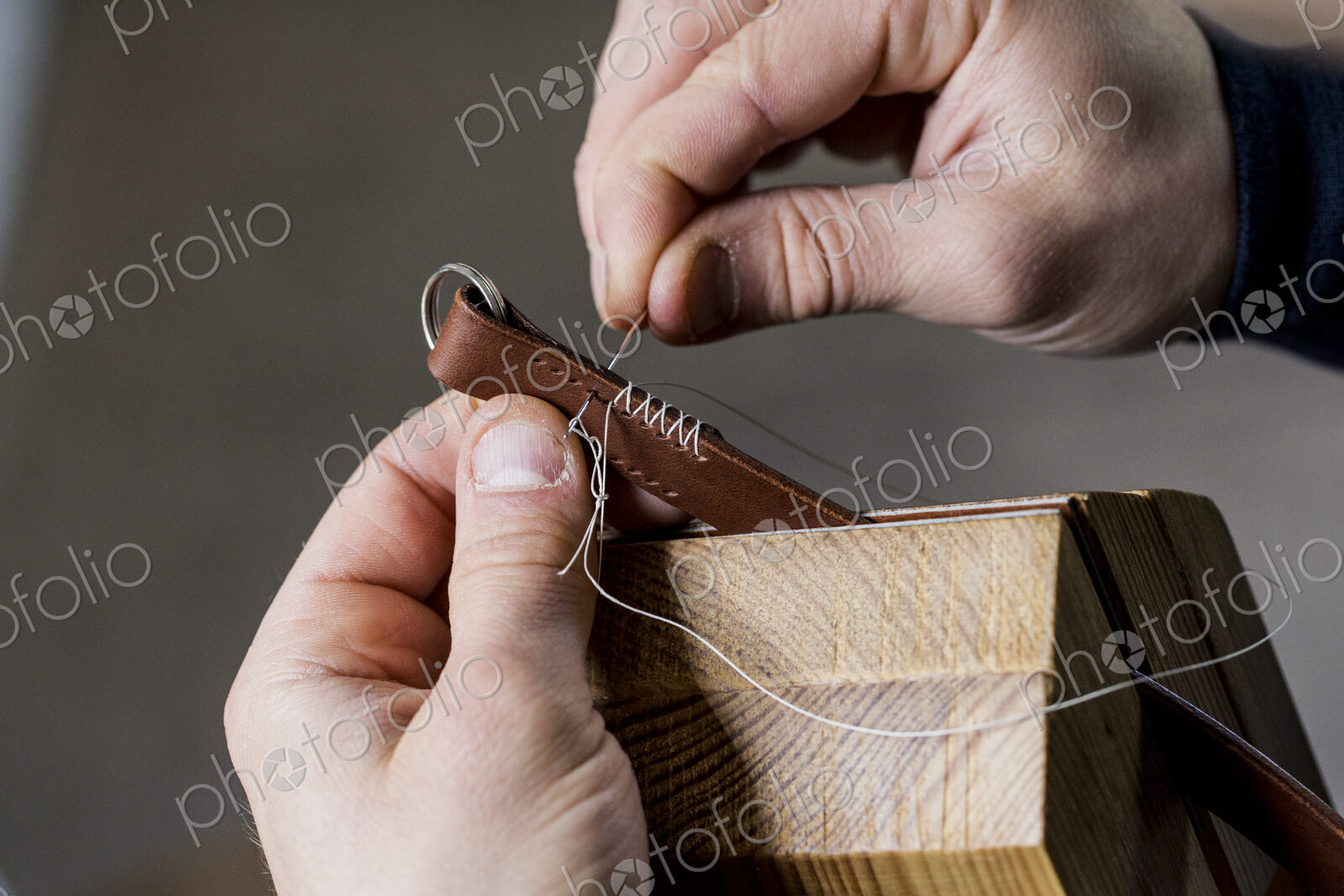Close up of craftsman making brown leather camera strap, hand stitching two pieces of…