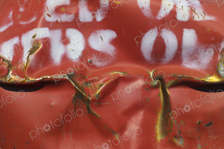 Close up of dented and rusty old red metal oil drum with white lettering.
