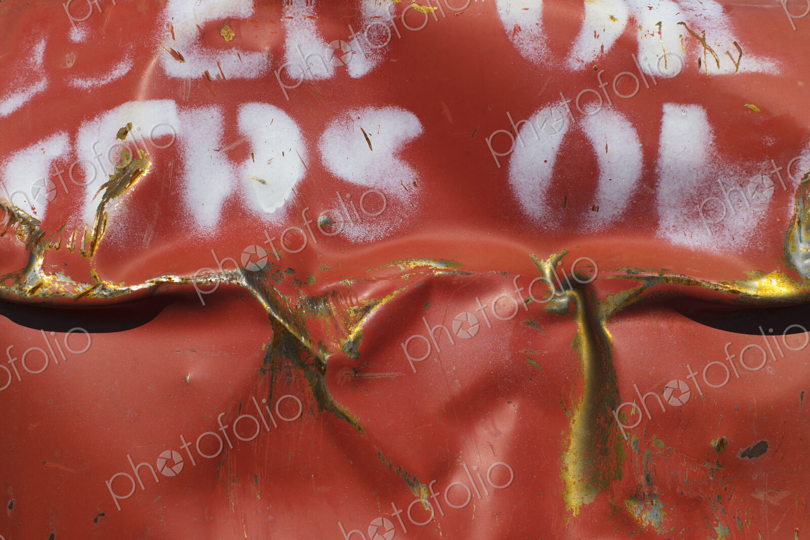 Close up of dented and rusty old red metal oil drum with white lettering.