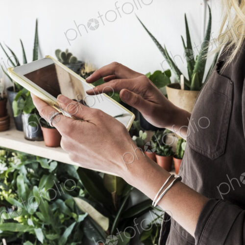 Close up of female owner of plant shop holding digital tablet, a selection of plants… Close up of female owner of plant shop holding digital tablet, a selection of plants…