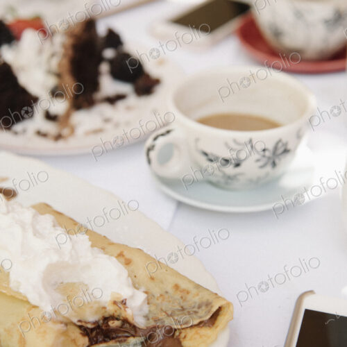 Close up of food and drink on a table, a hot drink, cake and pancake with cream. Close up of food and drink on a table, a hot drink, cake and pancake with cream.