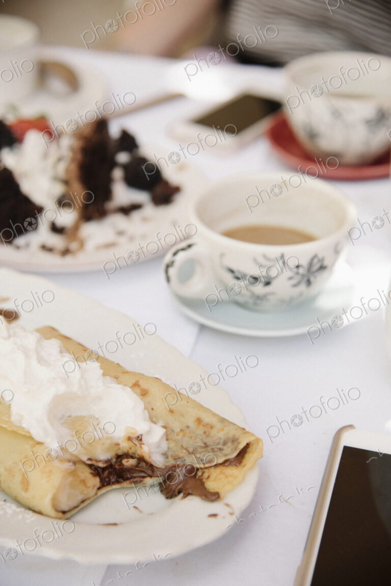 Close up of food and drink on a table, a hot drink, cake and pancake with cream.