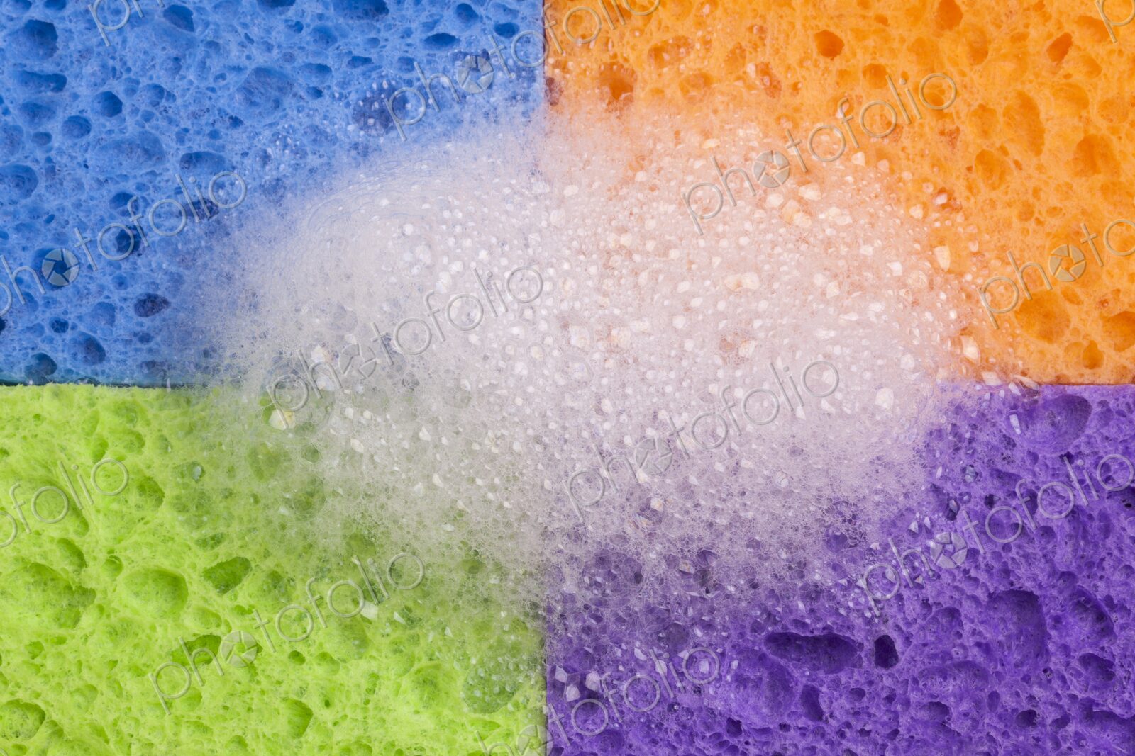 Close-up of four brightly colored household sponges arranged in a grid formation with…