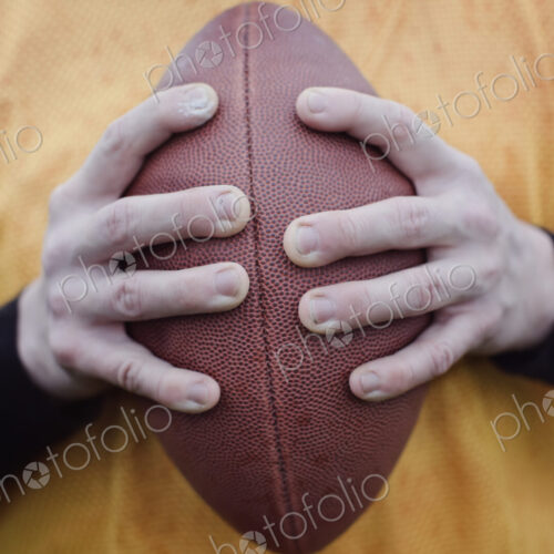 Close up of hands holding an American football.