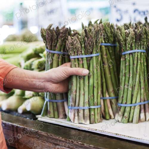 Close up of human hand holding bunch of fresh green asparagus at a fruit and vegetable… Close up of human hand holding bunch of fresh green asparagus at a fruit and vegetable…