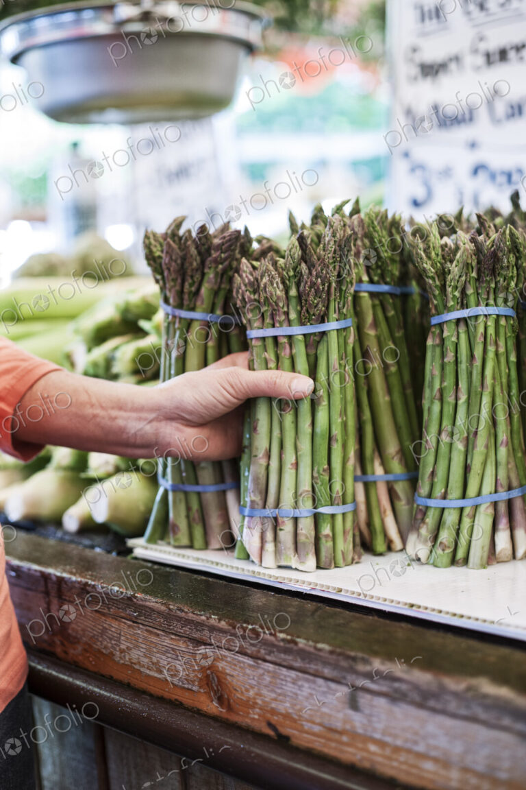 Close up of human hand holding bunch of fresh green asparagus at a fruit and vegetable…