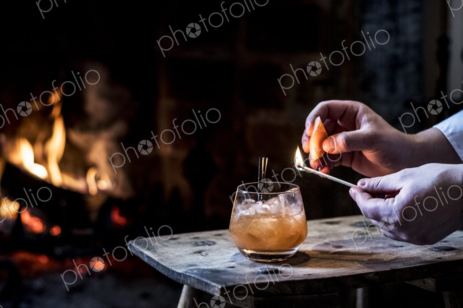 Close up of human hand striking match over glass with alcoholic drink.