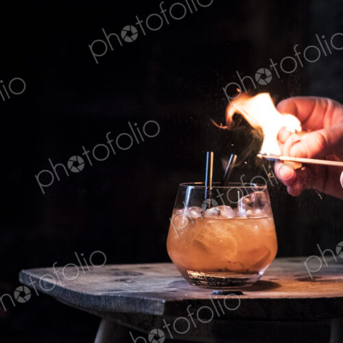 Close up of human hand striking match over glass with alcoholic drink. Close up of human hand striking match over glass with alcoholic drink.