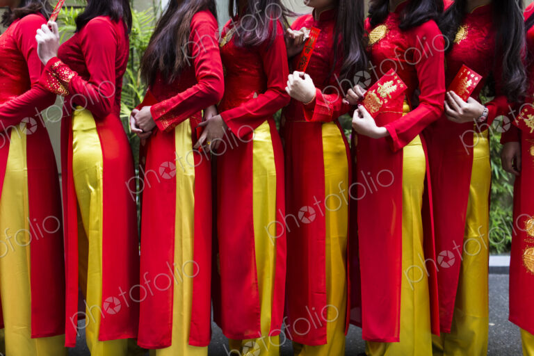 Close up of line of young women in traditional red and yellow dress outside of a wedding.