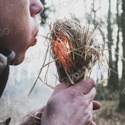 Close up of man blowing on bundle of straw, igniting fire.