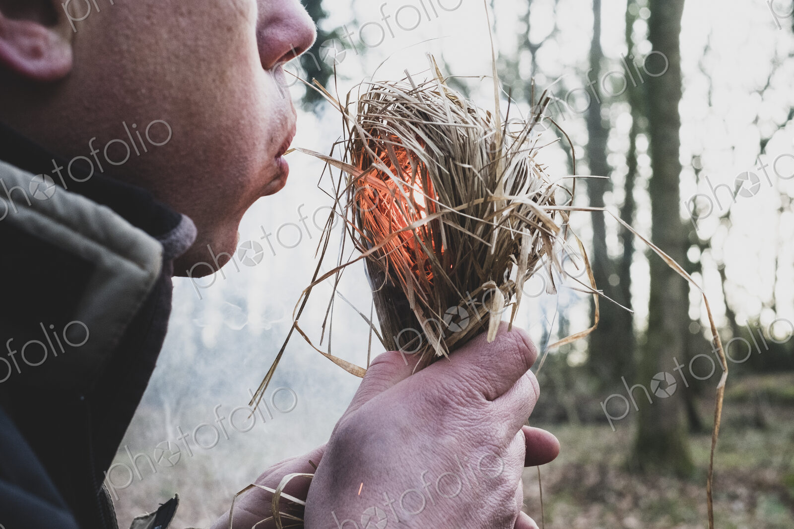 Close up of man blowing on bundle of straw, igniting fire.