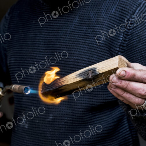 Close up of man holding blowtorch, charring wooden handle of a knife. Close up of man holding blowtorch, charring wooden handle of a knife.