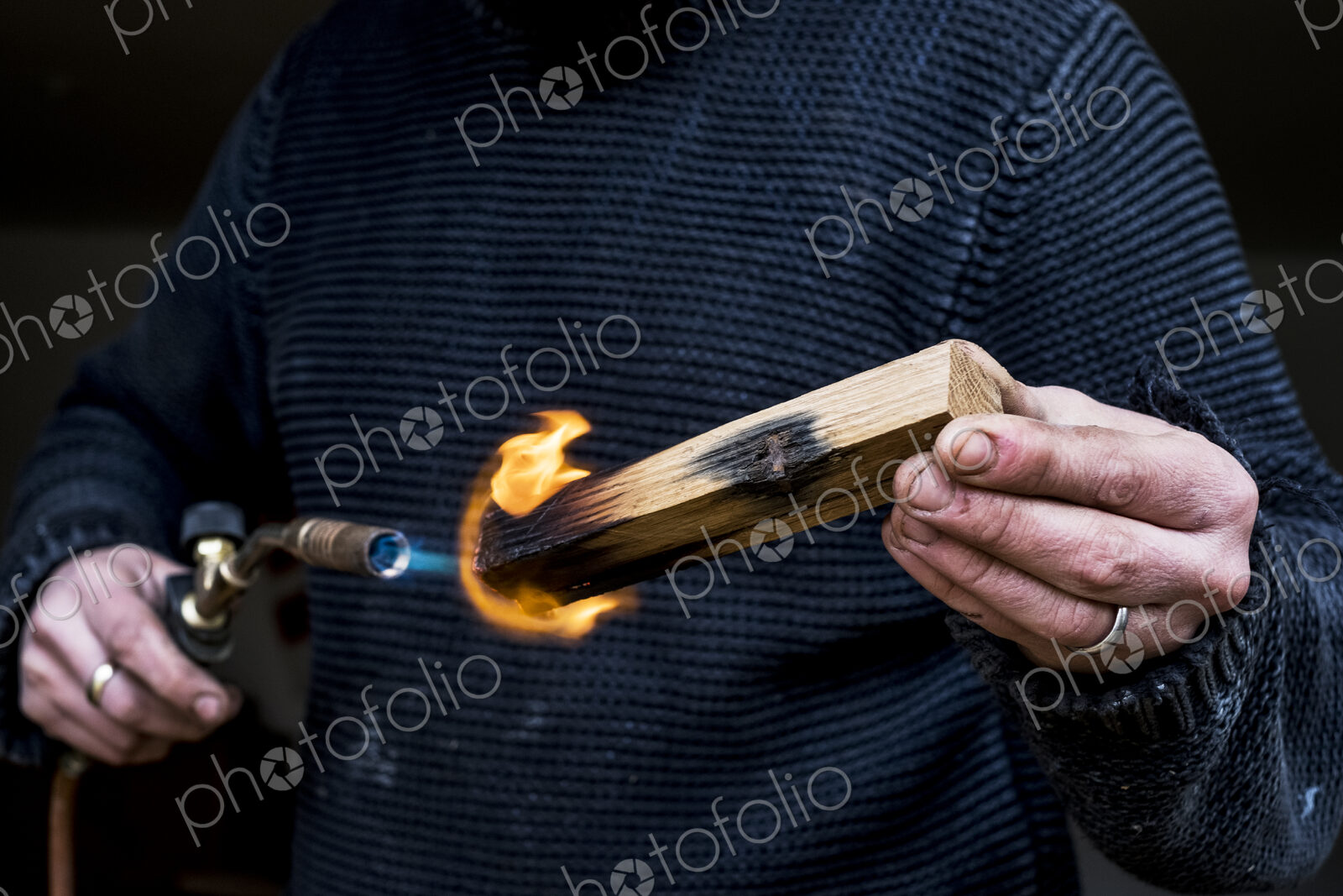 Close up of man holding blowtorch, charring wooden handle of a knife.