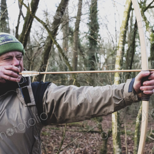 Close up of man standing in forest, using bow and arrow.