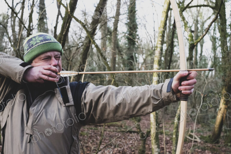 Close up of man standing in forest, using bow and arrow.