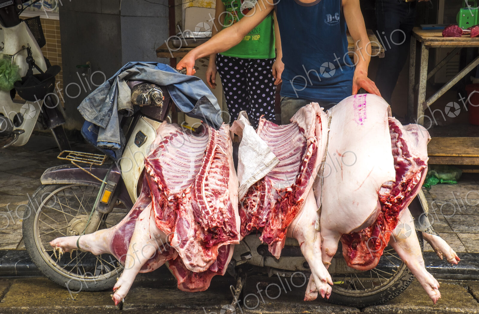 Close up of man transporting three pig carcasses on an old motor-scooter.