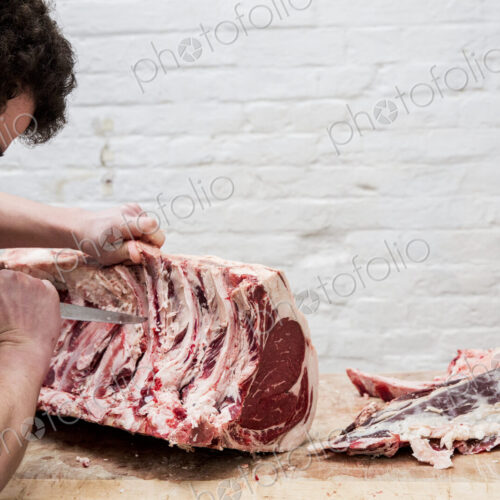Close up of man wearing apron standing at a wooden butcher's block, butchering beef…