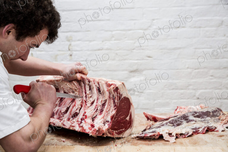 Close up of man wearing apron standing at a wooden butcher's block, butchering beef…
