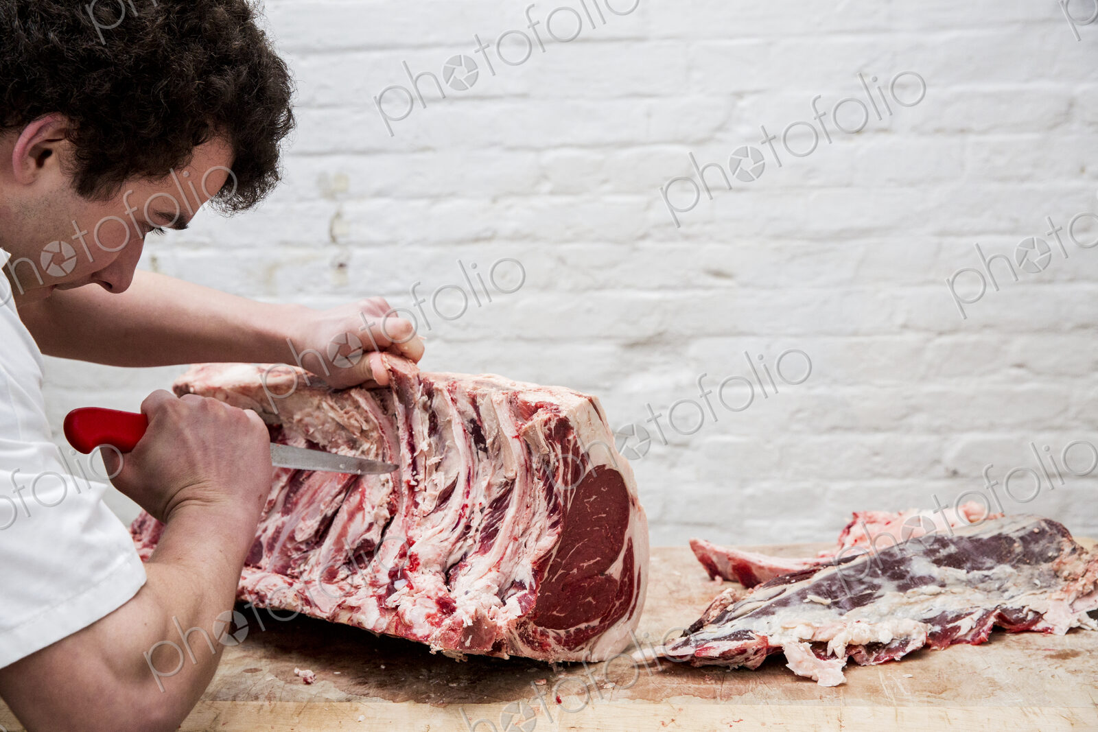 Close up of man wearing apron standing at a wooden butcher’s block, butchering beef…