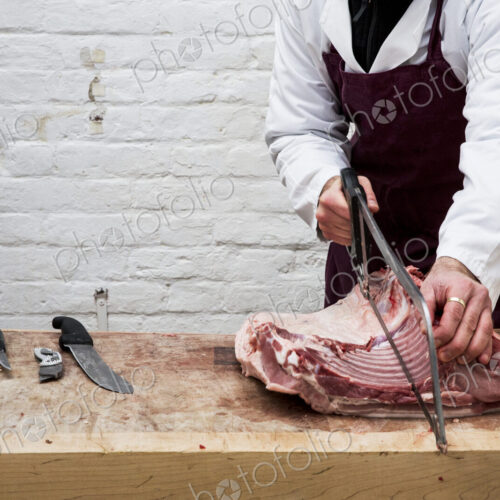 Close up of man wearing apron standing at a wooden butcher's block, butchering piece…
