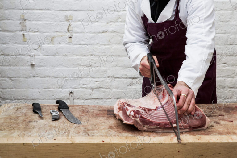 Close up of man wearing apron standing at a wooden butcher's block, butchering piece…