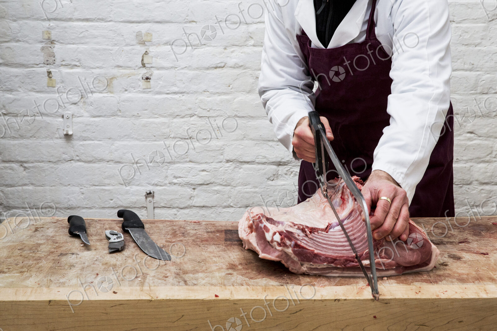 Close up of man wearing apron standing at a wooden butcher’s block, butchering piece…