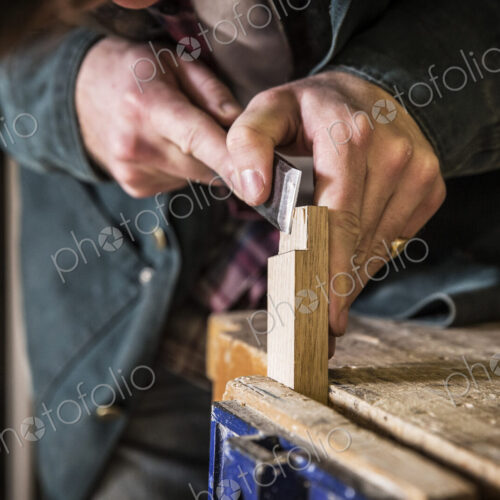 Close up of man working standing in a woodworking workshop, using chisel on piece of wood. Close up of man working standing in a woodworking workshop, using chisel on piece of wood.