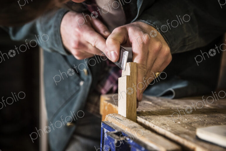 Close up of man working standing in a woodworking workshop, using chisel on piece of wood.