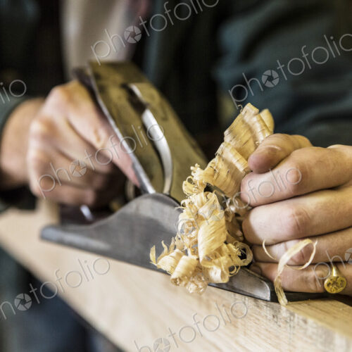 Close up of man working standing in a woodworking workshop, using plane on plank of wood.