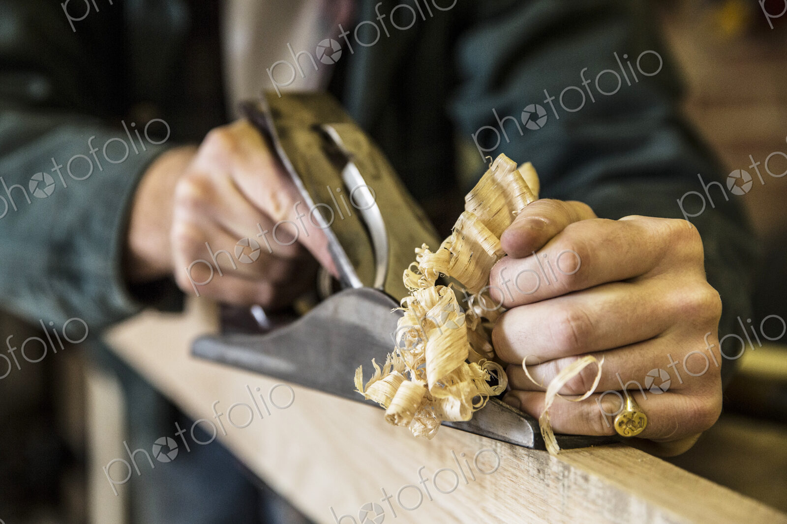 Close up of man working standing in a woodworking workshop, using plane on plank of wood.