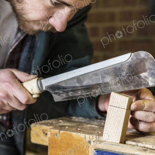 Close up of man working standing in a woodworking workshop, using saw on piece of wood. Close up of man working standing in a woodworking workshop, using saw on piece of wood.