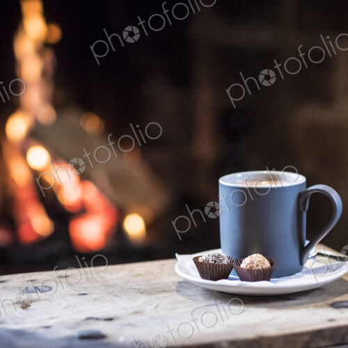 Close up of mug with hot drink on wooden table in front of fireplace. Close up of mug with hot drink on wooden table in front of fireplace.